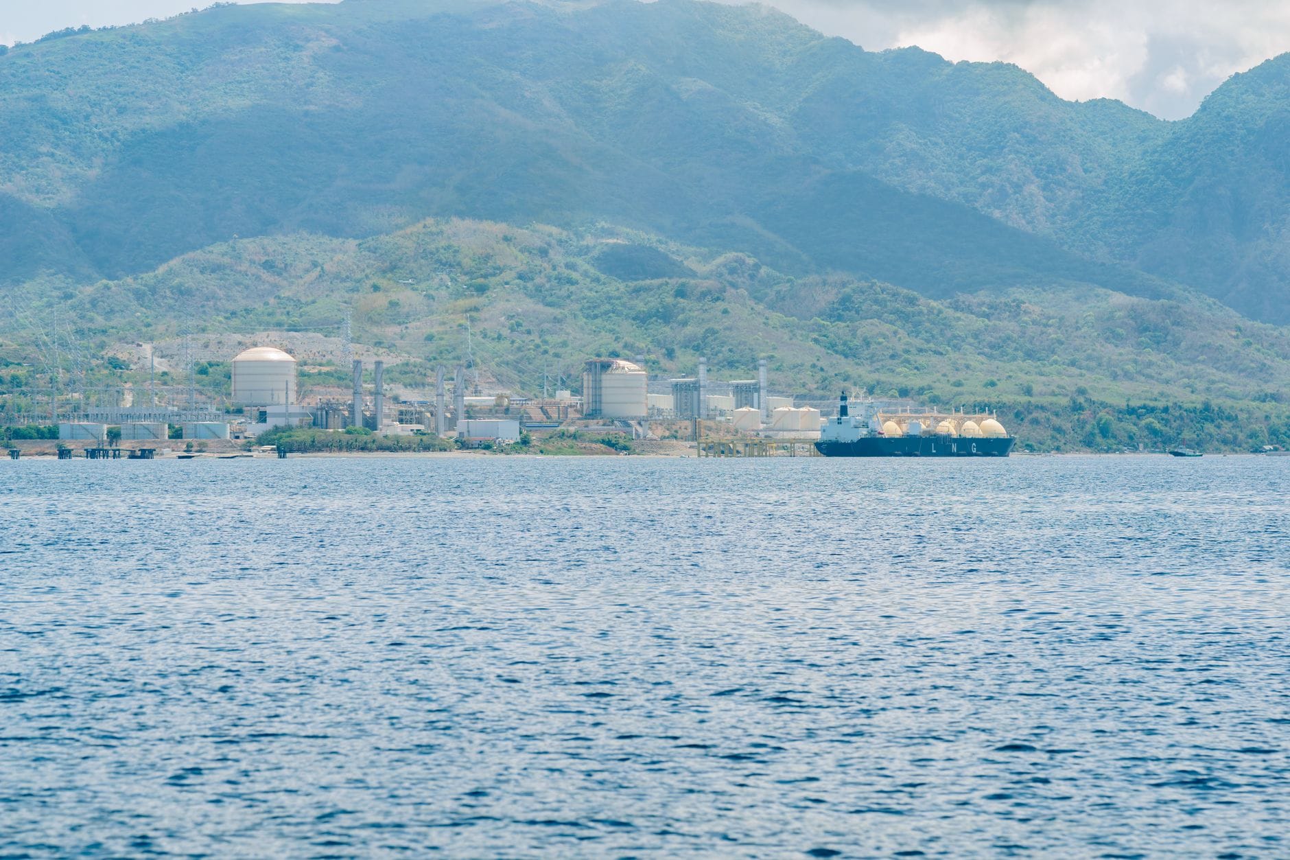 Terminal LNG na wybrzeżu z zacumowanym gazowcem na tle gór